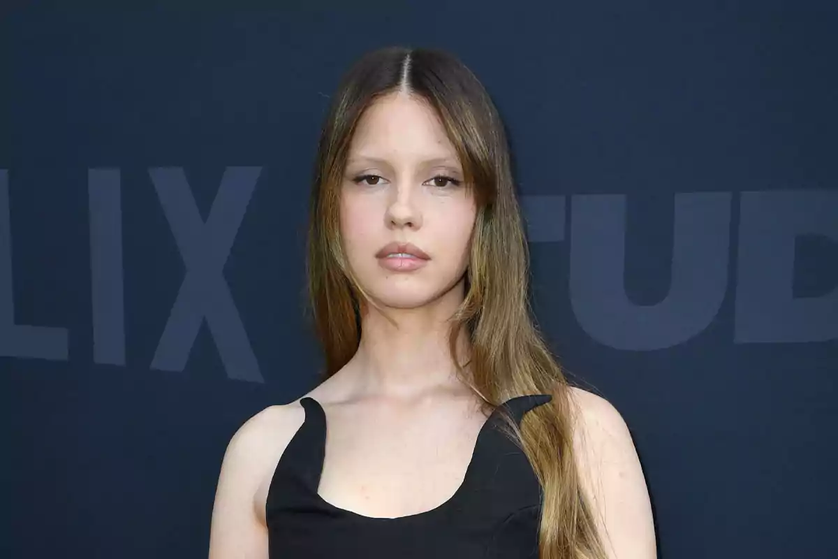Mujer joven de cabello largo y lacio con vestido negro posando frente a un fondo oscuro Mujer joven de cabello largo y lacio con vestido negro posando frente a un fondo oscuro