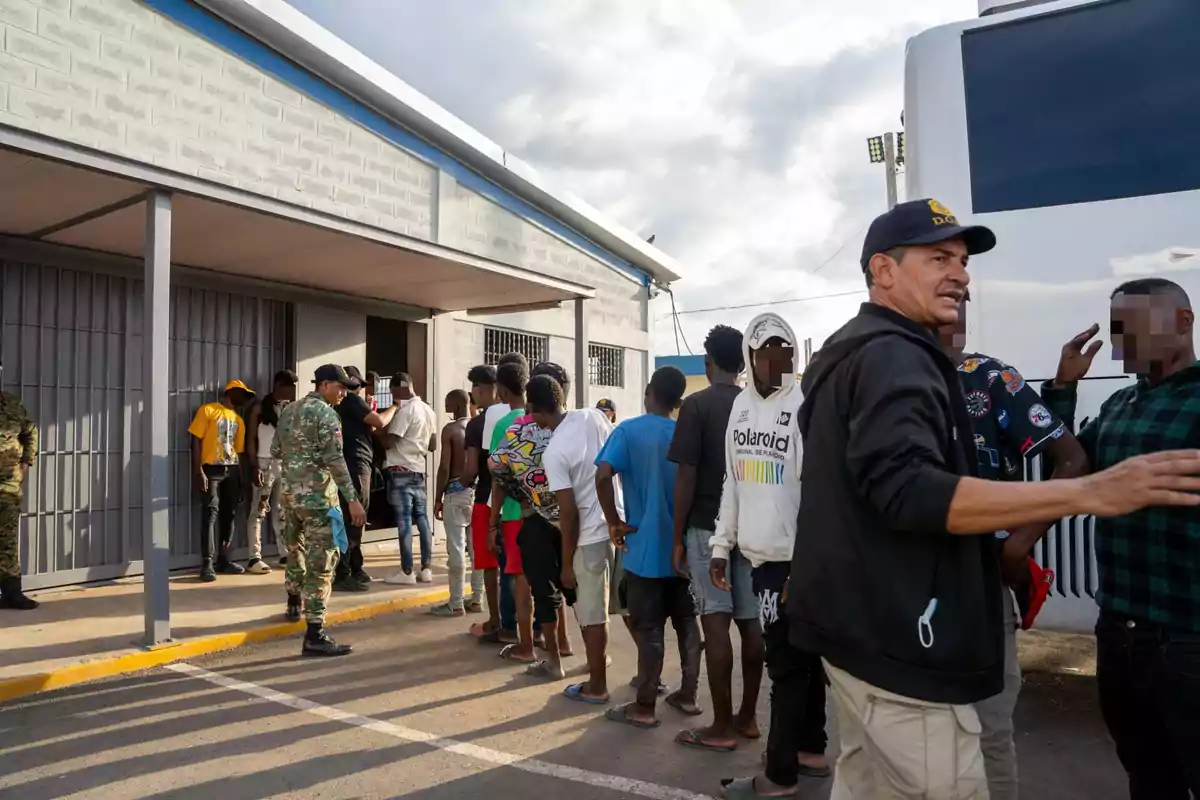 Personas haciendo fila afuera de un edificio mientras personal de seguridad supervisa la entrada