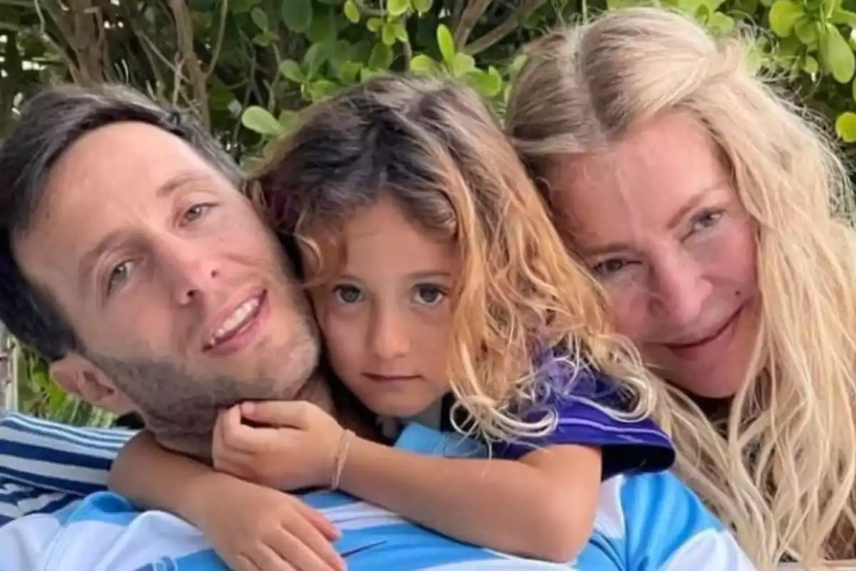 Una familia abrazada sonríe mientras posa al aire libre rodeada de vegetación.