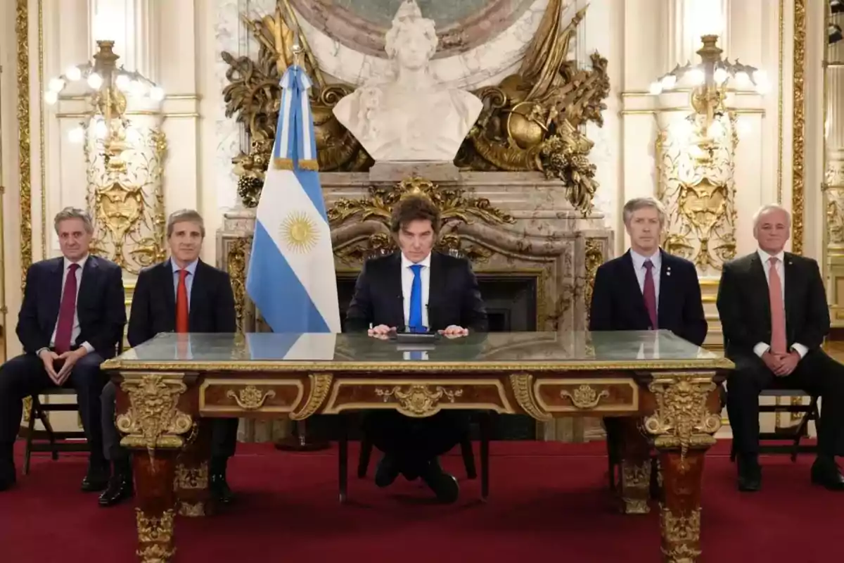 Cinco hombres con traje sentados en una sala elegante con una bandera de Argentina y una escultura al fondo Cinco hombres con traje sentados en una sala elegante con una bandera de Argentina y una escultura al fondo