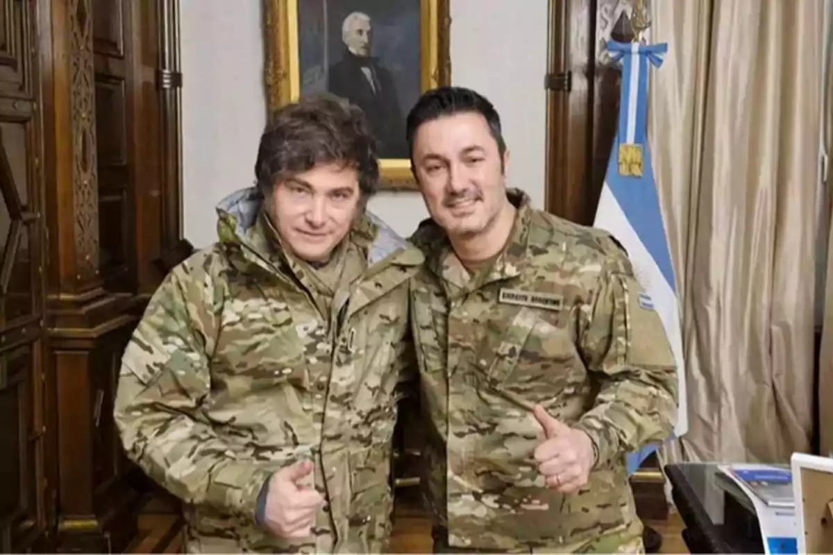 Two people in camouflage clothing pose smiling and giving a thumbs-up gesture in an office with an Argentine flag and a portrait on the wall. Two people in camouflage clothing pose smiling and giving a thumbs-up gesture in an office with an Argentine flag and a portrait on the wall.