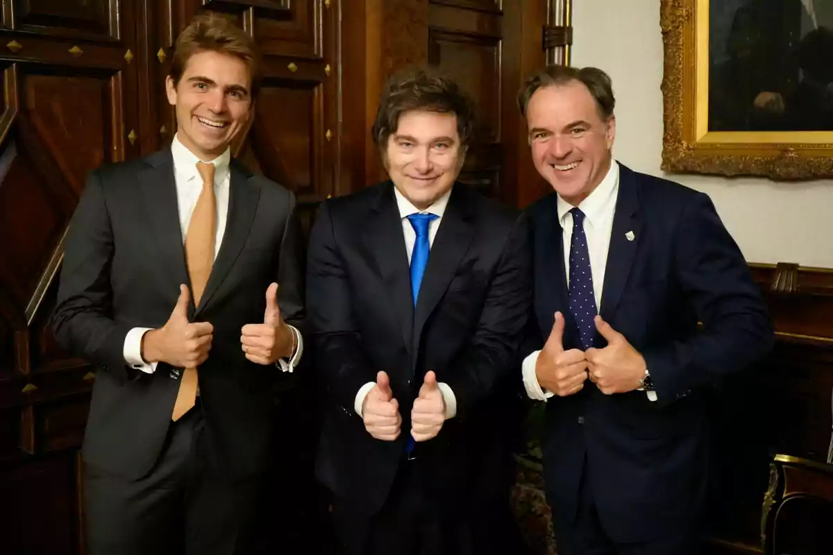 Three men dressed in suits smile and give two thumbs up in an elegant room with wooden walls. Three men dressed in suits smile and give two thumbs up in an elegant room with wooden walls.
