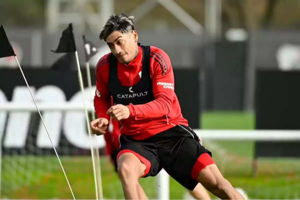 Futbolista entrenando en una cancha con banderines y usando ropa deportiva roja y negra Futbolista entrenando en una cancha con banderines y usando ropa deportiva roja y negra
