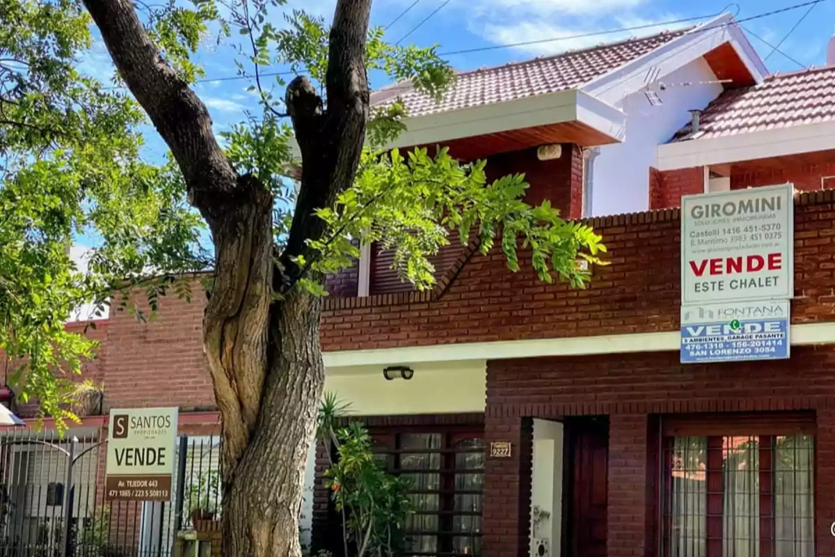 Brick house for sale with real estate signs on the facade and a large tree in the front. Brick house for sale with real estate signs on the facade and a large tree in the front.