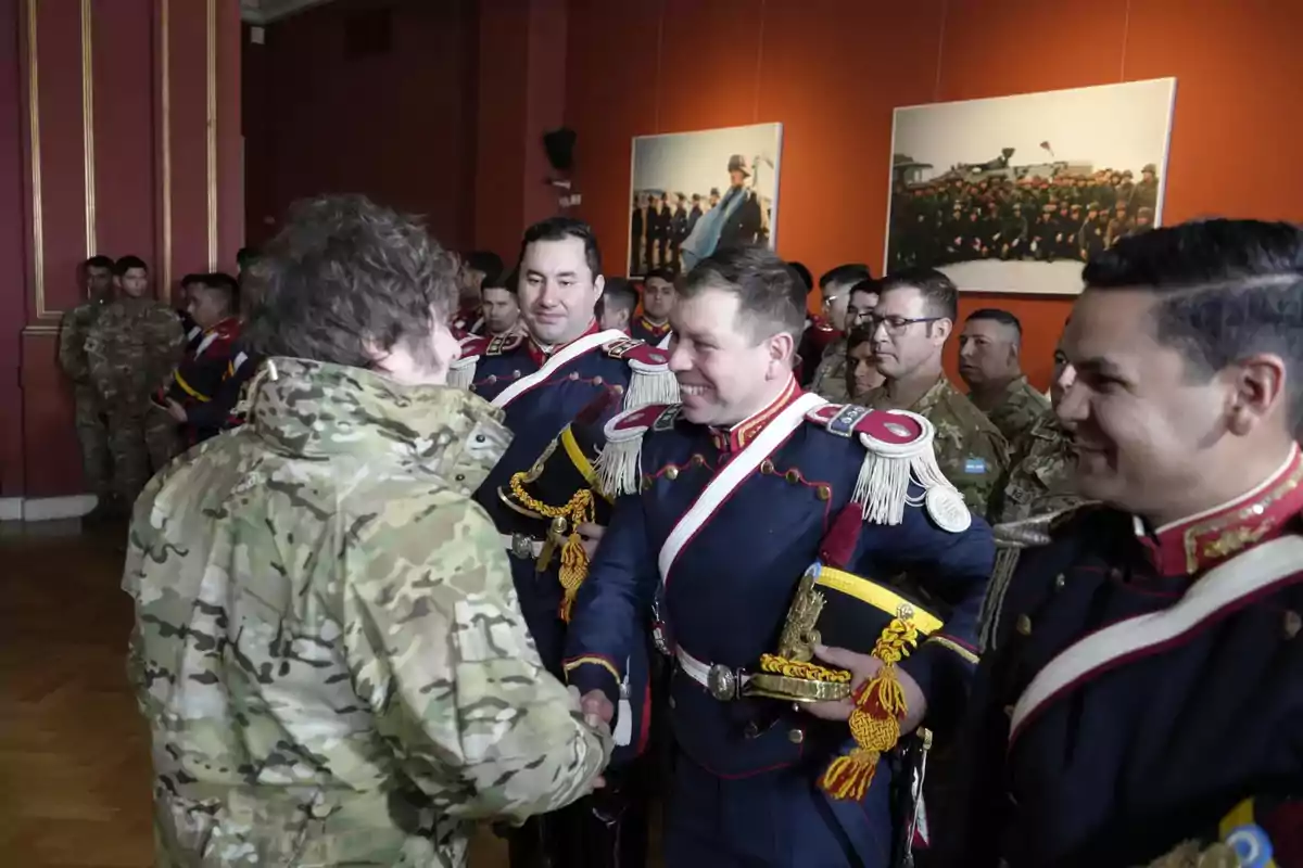 A man in a camouflage jacket greets a group of soldiers dressed in formal uniforms in a room decorated with paintings and red walls. A man in a camouflage jacket greets a group of soldiers dressed in formal uniforms in a room decorated with paintings and red walls.