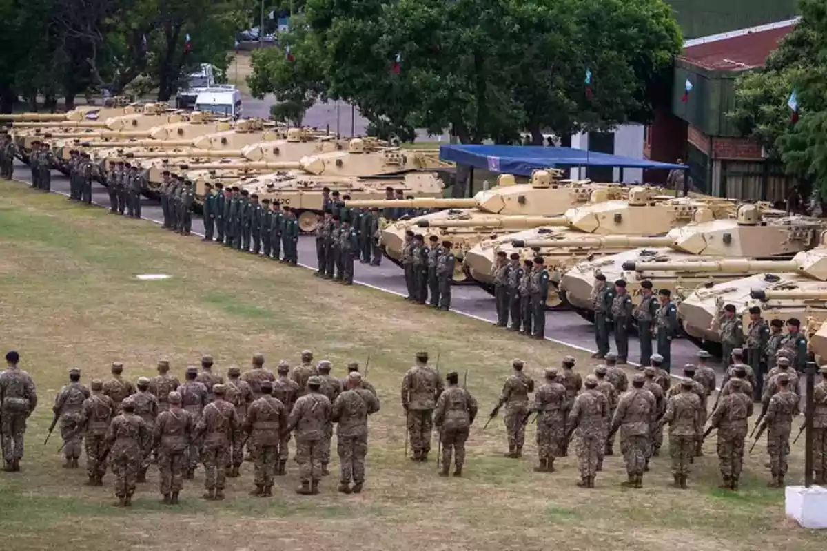 Soldiers lined up in front of a row of military tanks in an open field during a ceremony.