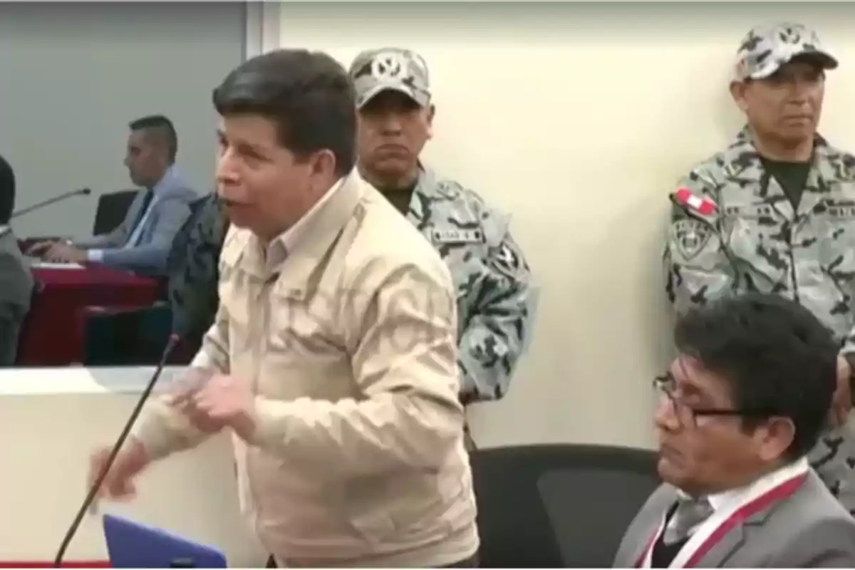 Un hombre de pie hablando frente a un micrófono en una sala con presencia de militares y otras personas sentadas Un hombre de pie hablando frente a un micrófono en una sala con presencia de militares y otras personas sentadas