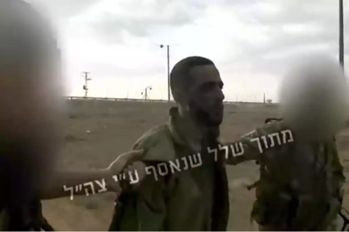 Soldier in military uniform being escorted by two people with blurred faces on arid terrain under a cloudy sky, with Hebrew text over the image. Soldier in military uniform being escorted by two people with blurred faces on arid terrain under a cloudy sky, with Hebrew text over the image.