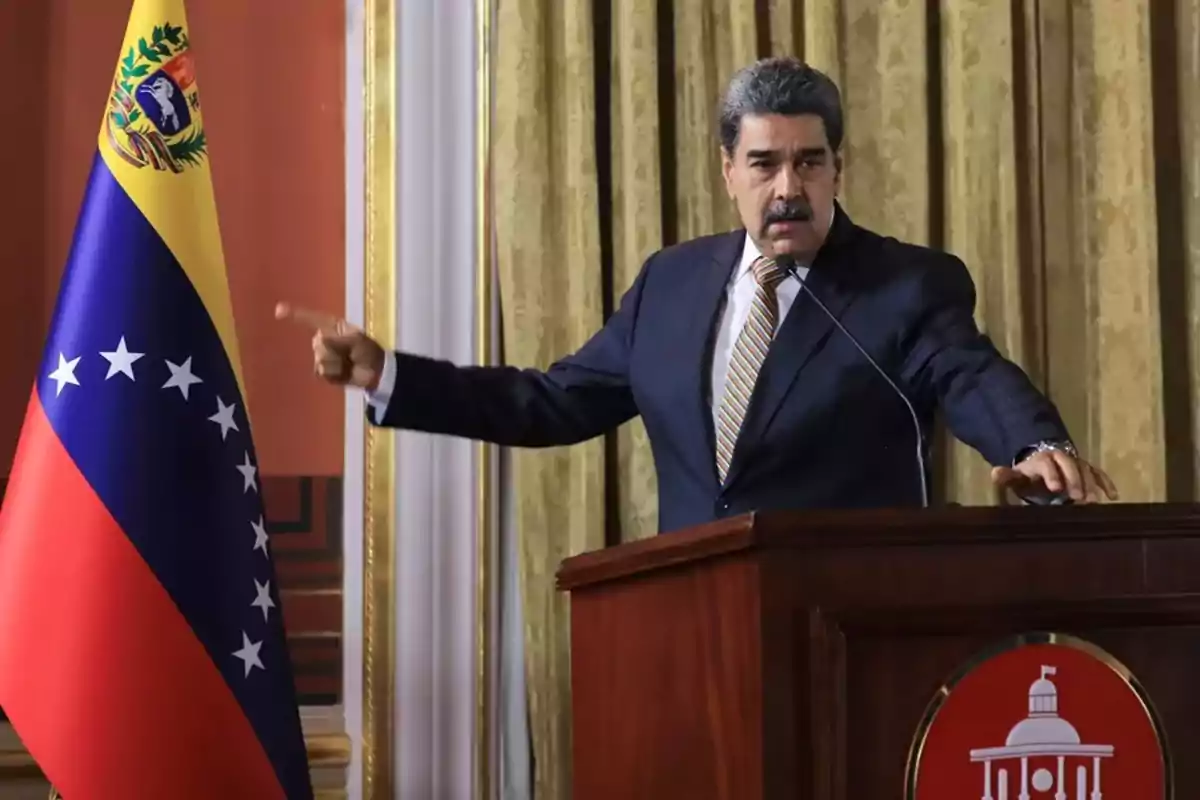 Man in a suit speaking at a podium next to a Venezuelan flag Man in a suit speaking at a podium next to a Venezuelan flag