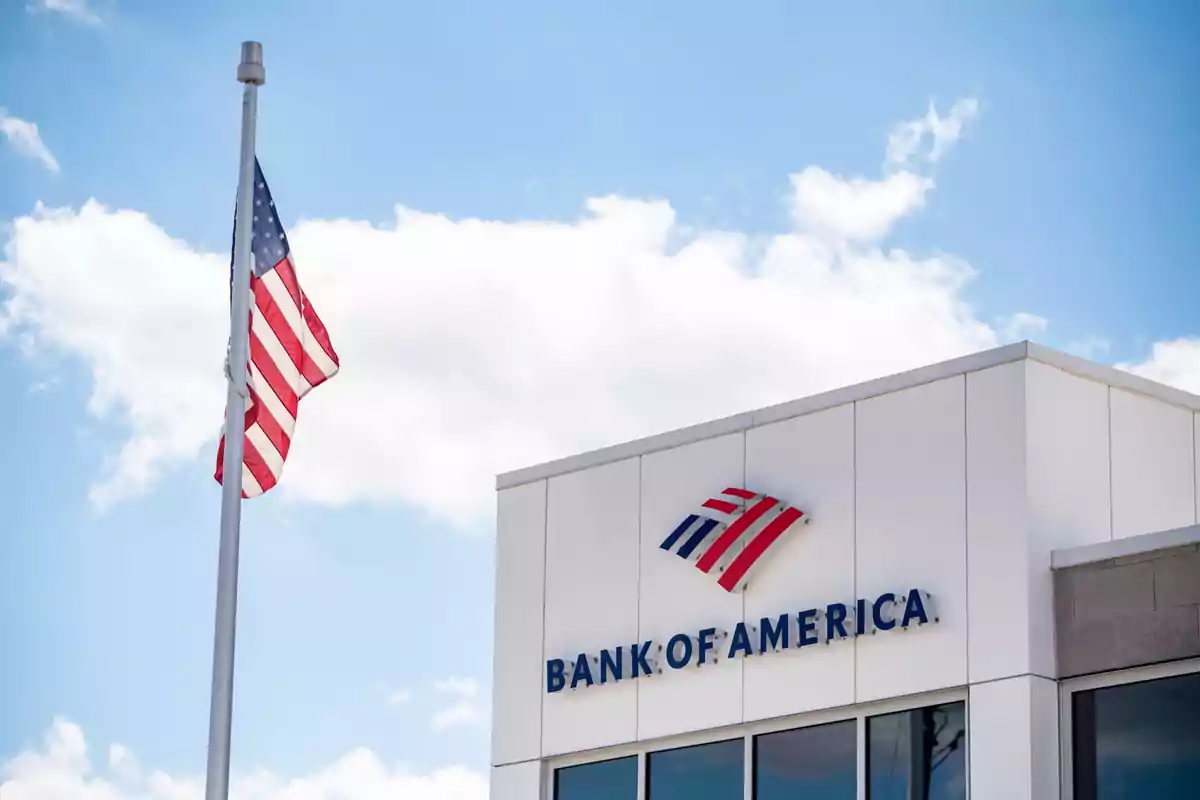 Facade of a Bank of America branch with a United States flag waving in front of the building on a sunny day