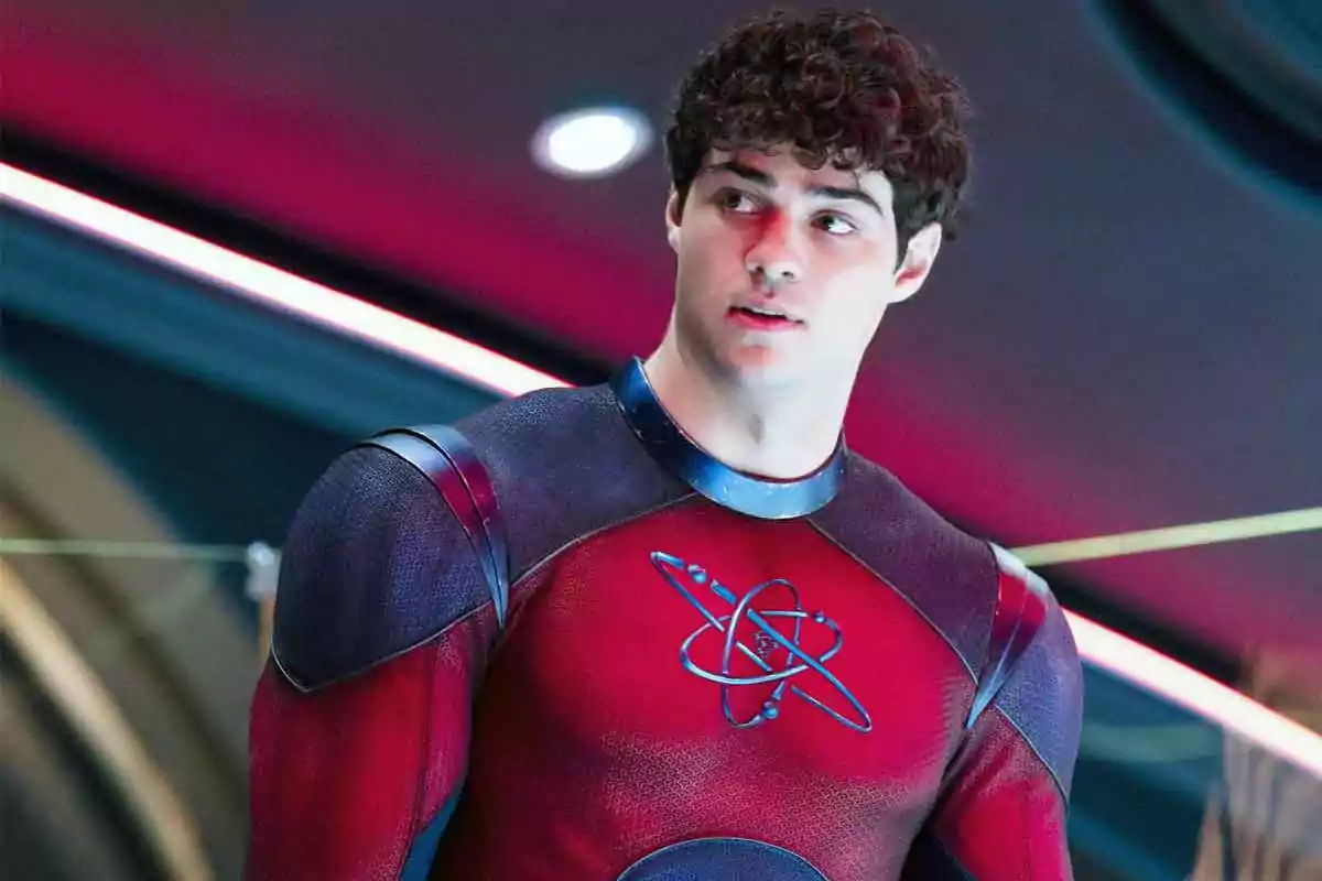 Joven con cabello rizado usando un traje de superhéroe rojo con un símbolo de átomo en el pecho en un entorno futurista