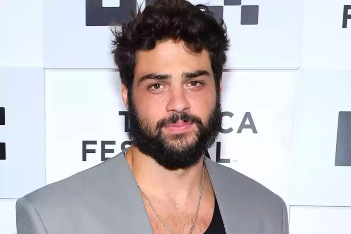 Hombre de cabello oscuro y barba posando frente a un fondo con logotipos en un evento.