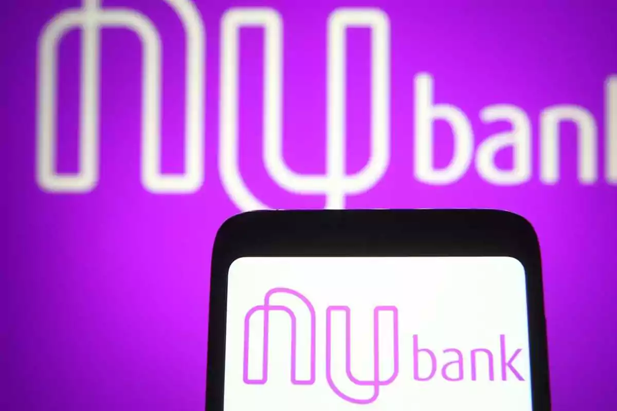 Logo de Nubank en color morado mostrado en la pantalla de un celular frente a un fondo del mismo logo ampliado Logo de Nubank en color morado mostrado en la pantalla de un celular frente a un fondo del mismo logo ampliado