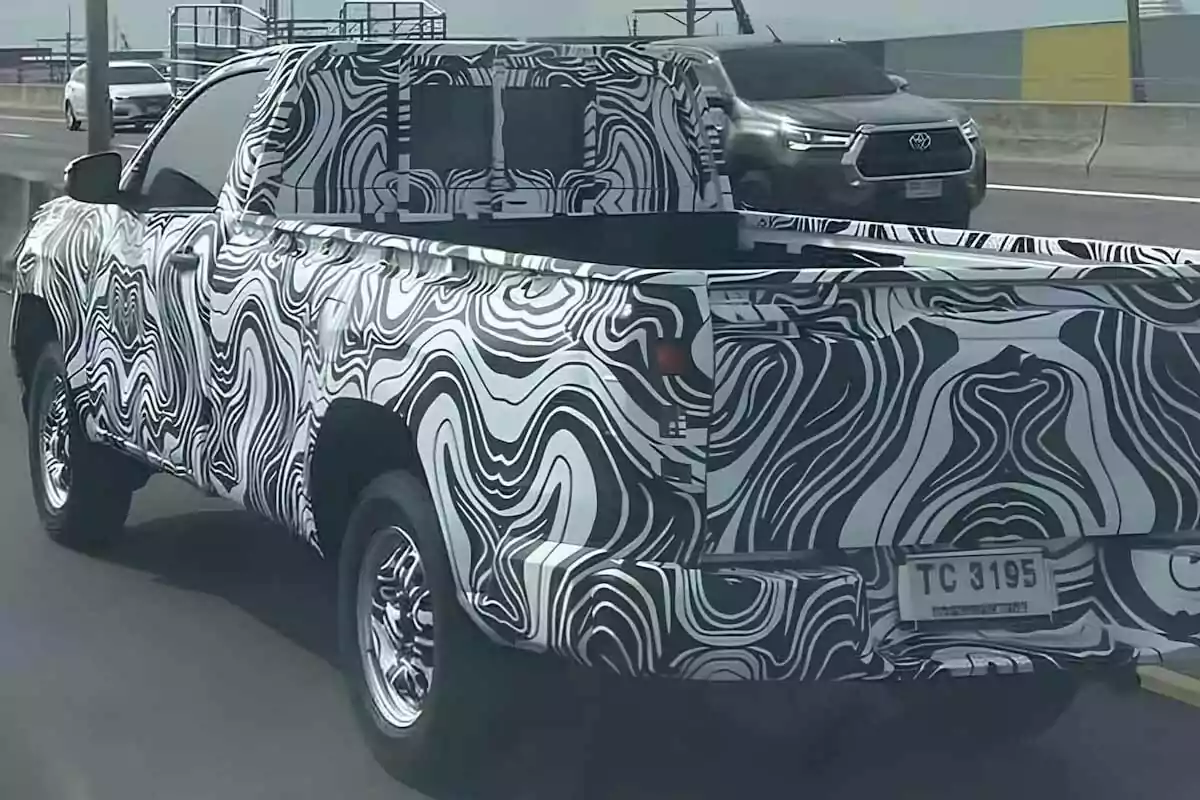 Una camioneta cubierta con camuflaje de patrones en blanco y negro circula por una carretera junto a otros vehículos. Una camioneta cubierta con camuflaje de patrones en blanco y negro circula por una carretera junto a otros vehículos.