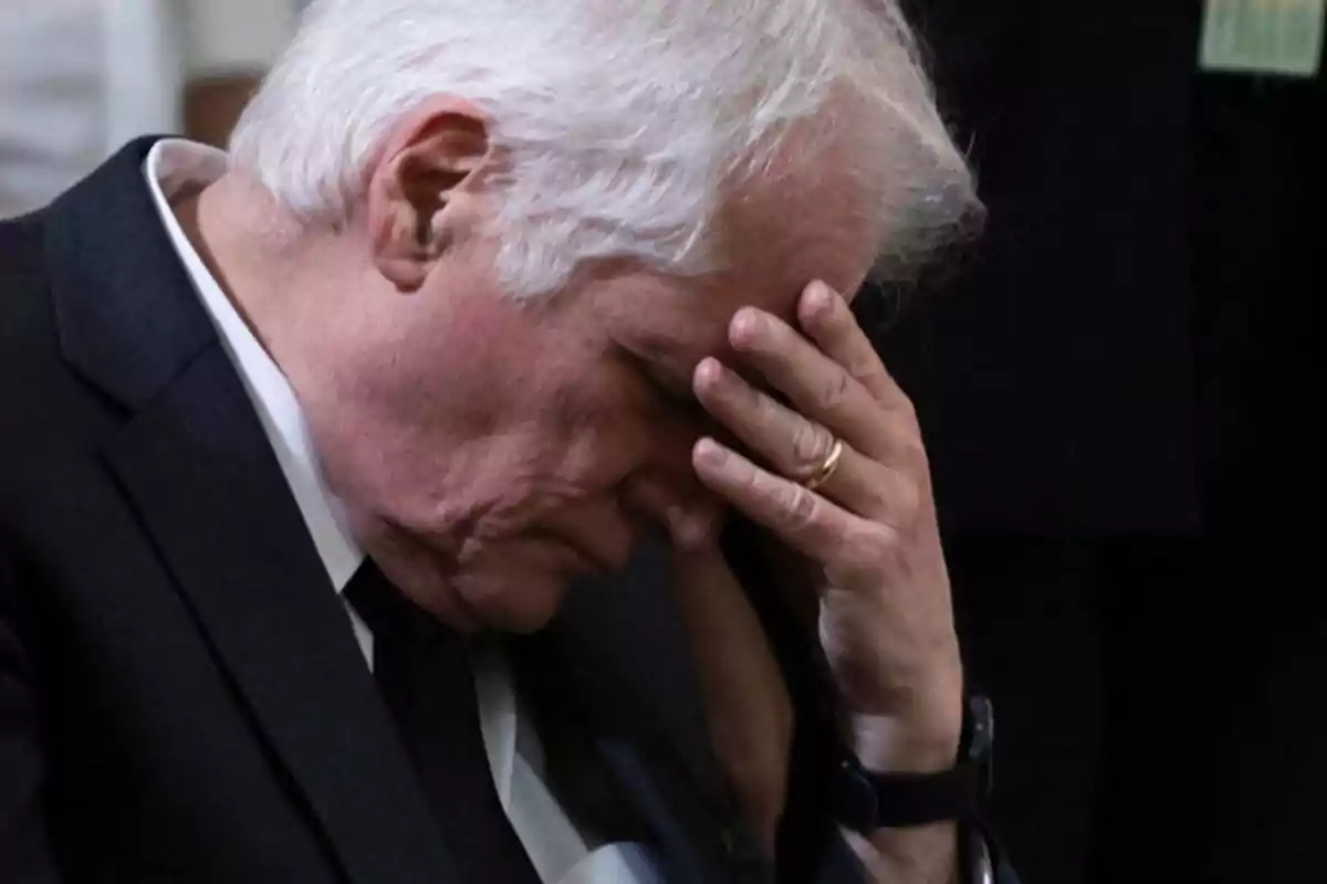 Elderly man with gray hair and a sad expression covering his face with one hand Elderly man with gray hair and a sad expression covering his face with one hand