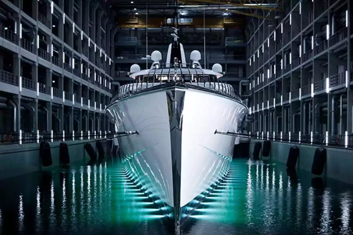 Yate de lujo iluminado en un astillero moderno rodeado de estructuras metálicas y luces reflejadas en el agua