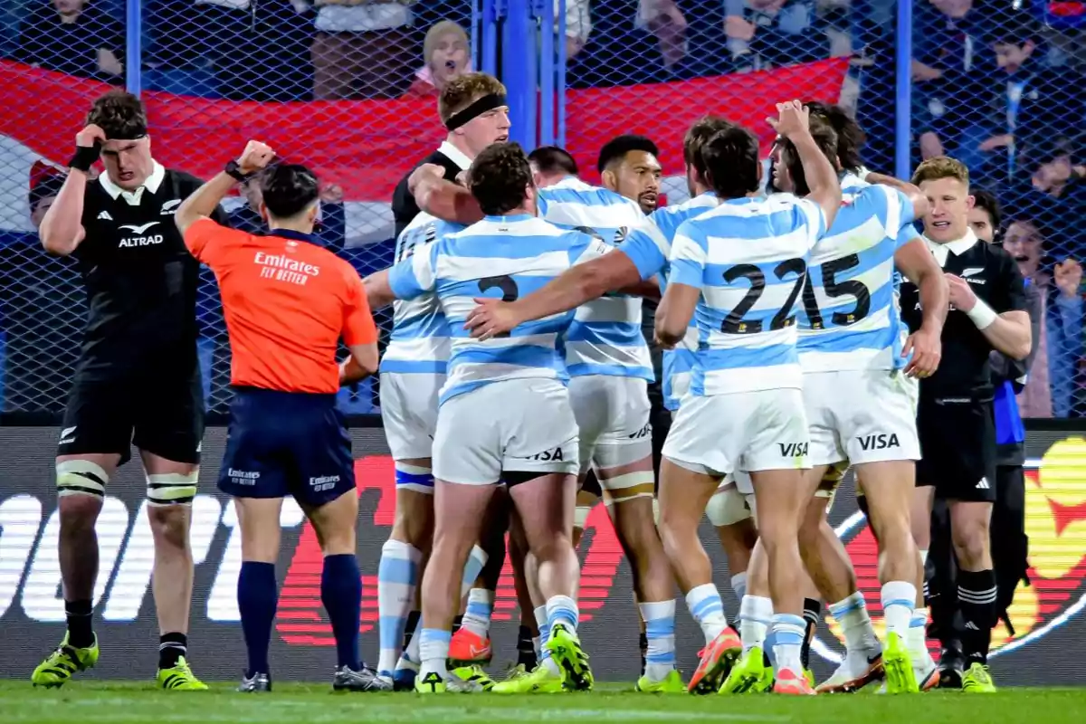 Argentina rugby players celebrate a try while a referee and New Zealand players watch on the field.
