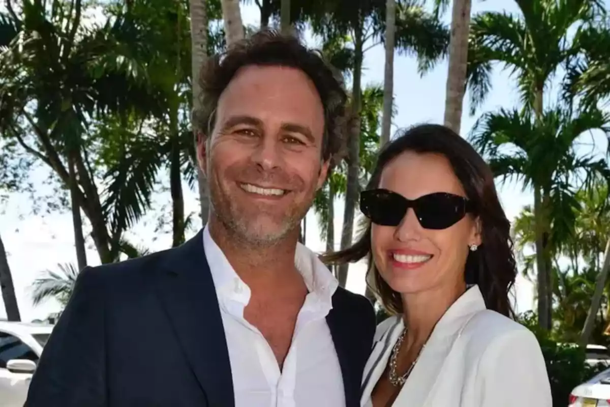 Pareja sonriente vestida de manera elegante posando al aire libre con palmeras de fondo Pareja sonriente vestida de manera elegante posando al aire libre con palmeras de fondo