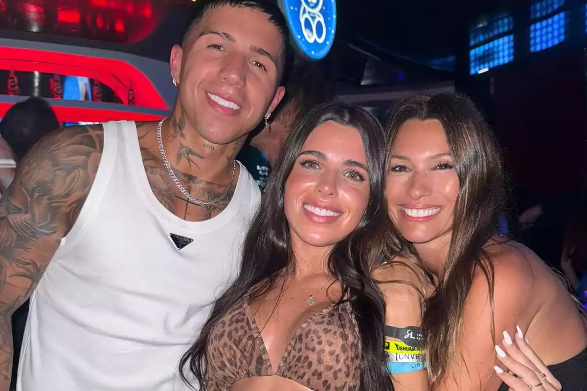 Tres personas sonríen y posan juntas en un club nocturno con luces de colores de fondo Tres personas sonríen y posan juntas en un club nocturno con luces de colores de fondo