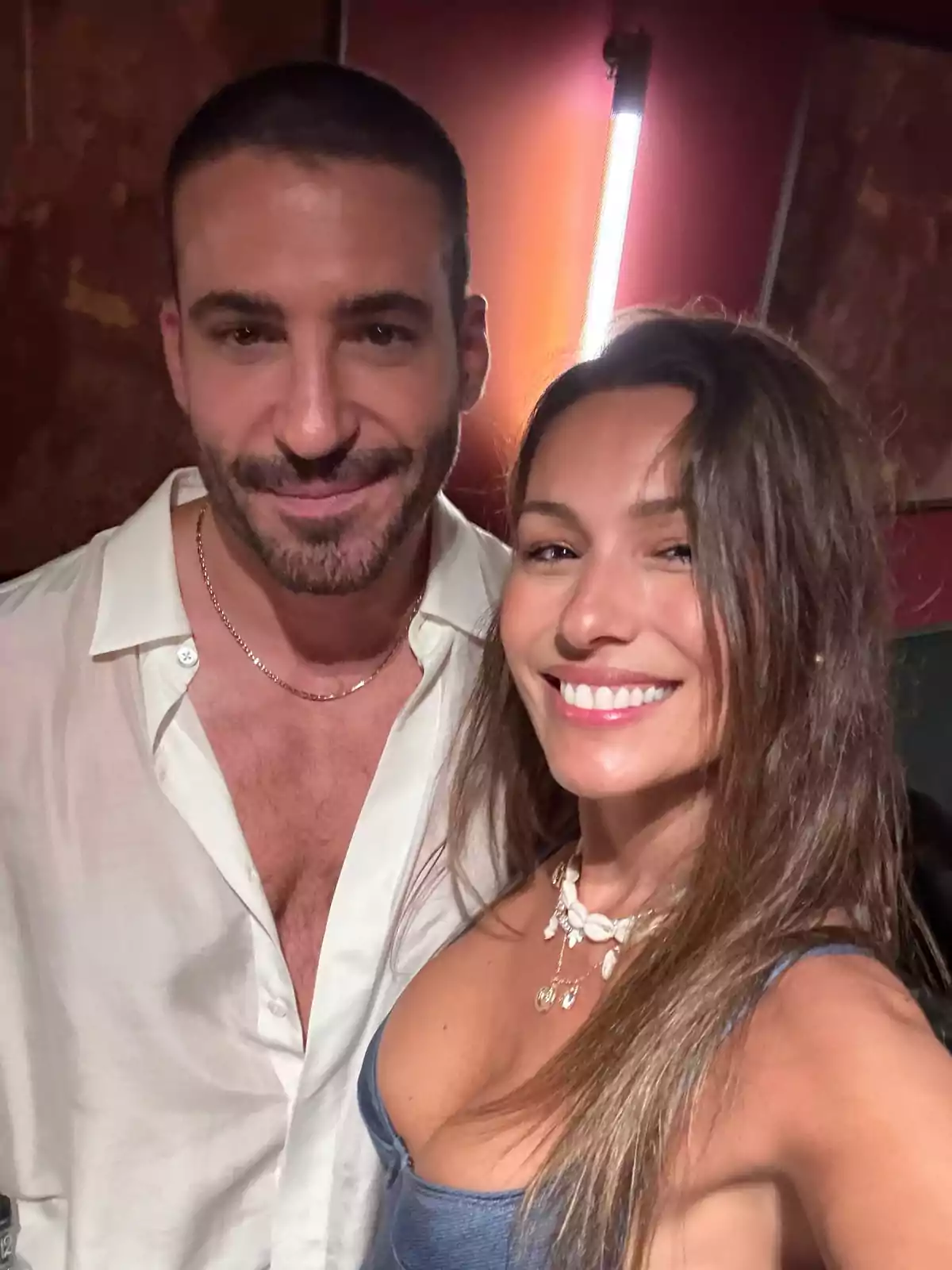 Una pareja sonríe mientras posa para una selfie en un ambiente interior con luz cálida de fondo Una pareja sonríe mientras posa para una selfie en un ambiente interior con luz cálida de fondo