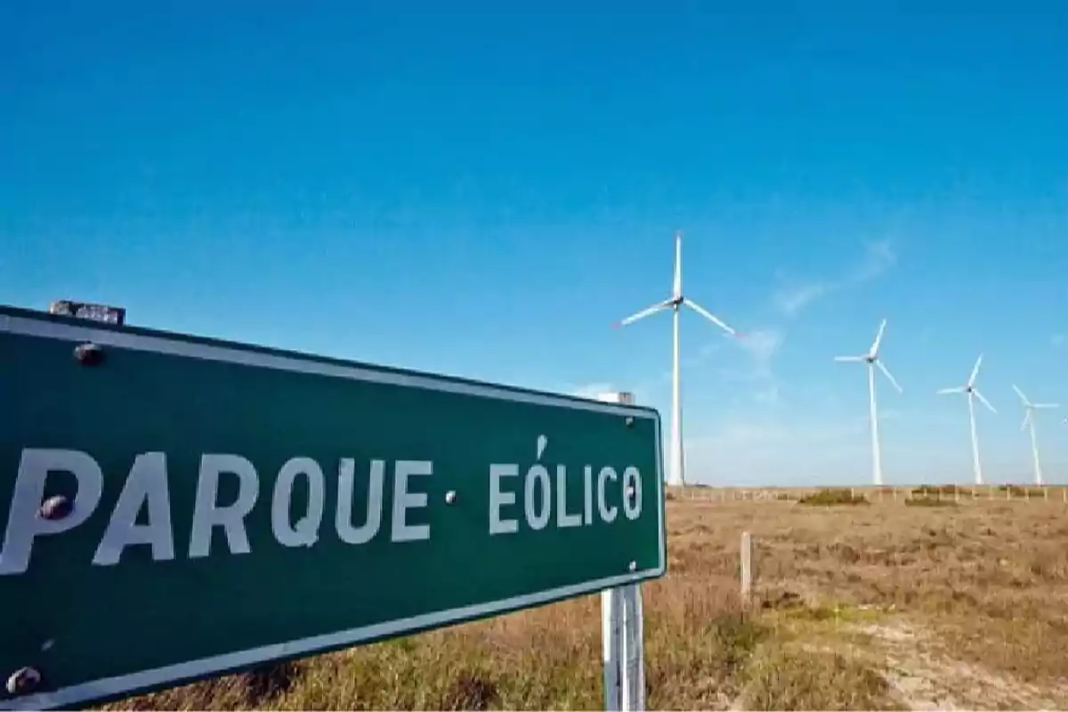 Letrero verde con la frase parque eólico y varios aerogeneradores en un campo bajo un cielo azul