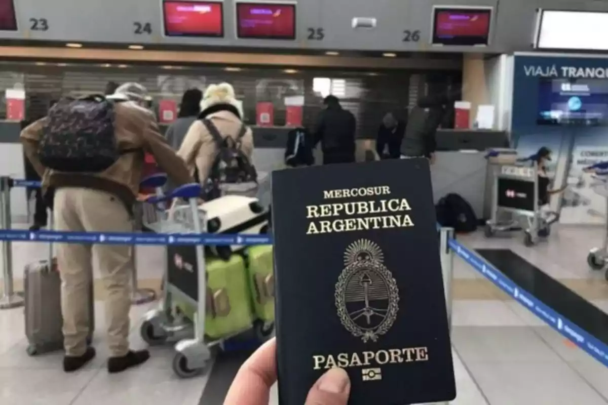 Persona sosteniendo un pasaporte argentino en un aeropuerto con gente haciendo fila y maletas en carritos