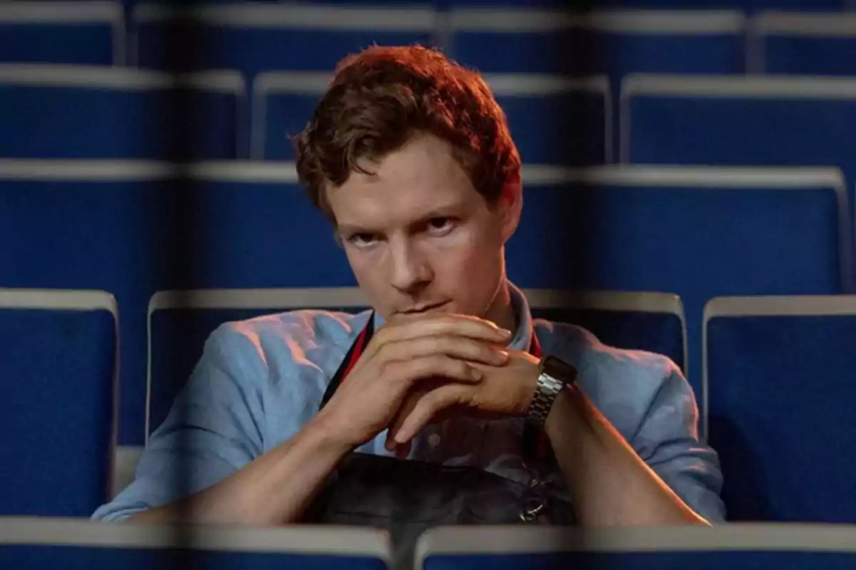 Young man sitting in a blue armchair with a serious expression and his hands clasped in front of his face Young man sitting in a blue armchair with a serious expression and his hands clasped in front of his face