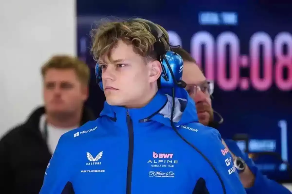 Joven con chaqueta azul de Alpine y auriculares en un ambiente de equipo de Fórmula 1 Joven con chaqueta azul de Alpine y auriculares en un ambiente de equipo de Fórmula 1