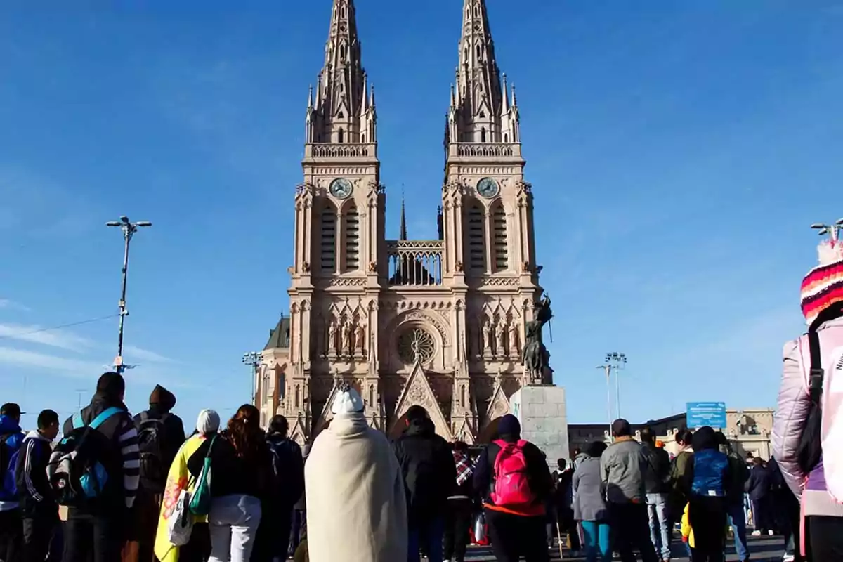A group of people is standing in front of a Gothic-style cathedral with two tall towers under a clear sky. A group of people is standing in front of a Gothic-style cathedral with two tall towers under a clear sky.
