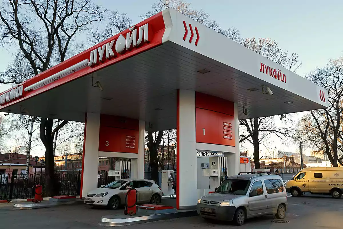 Lukoil gas station with several cars refueling in an urban setting and leafless trees in the background Lukoil gas station with several cars refueling in an urban setting and leafless trees in the background