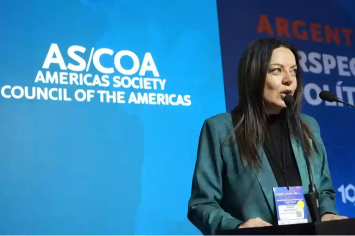 Woman speaking at a podium during an Americas Society Council of the Americas event with a blue background and white letters
