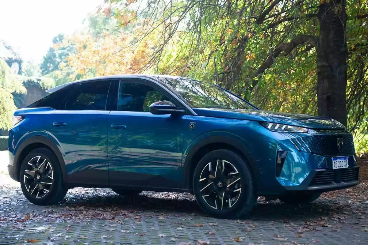 Auto SUV azul estacionado sobre un camino de adoquines rodeado de árboles con hojas otoñales Auto SUV azul estacionado sobre un camino de adoquines rodeado de árboles con hojas otoñales