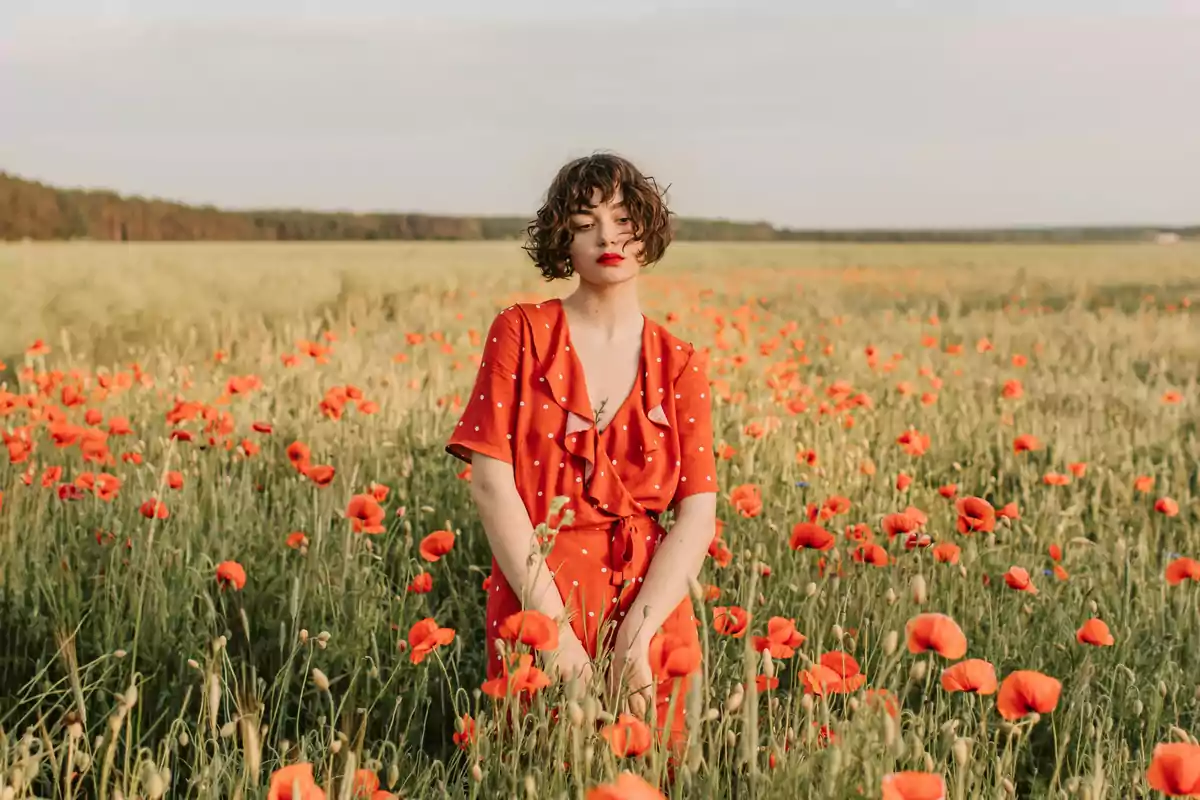 Mujer de cabello corto y rizado con vestido rojo de lunares blancos posando en un campo de amapolas Mujer de cabello corto y rizado con vestido rojo de lunares blancos posando en un campo de amapolas