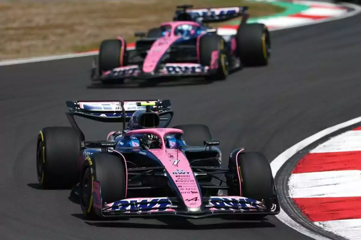 Two pink and blue Formula 1 cars are racing around a corner on a racetrack. Two pink and blue Formula 1 cars are racing around a corner on a racetrack.