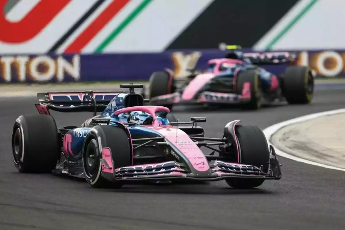 Two pink and blue Formula 1 cars race on a track during a competition.