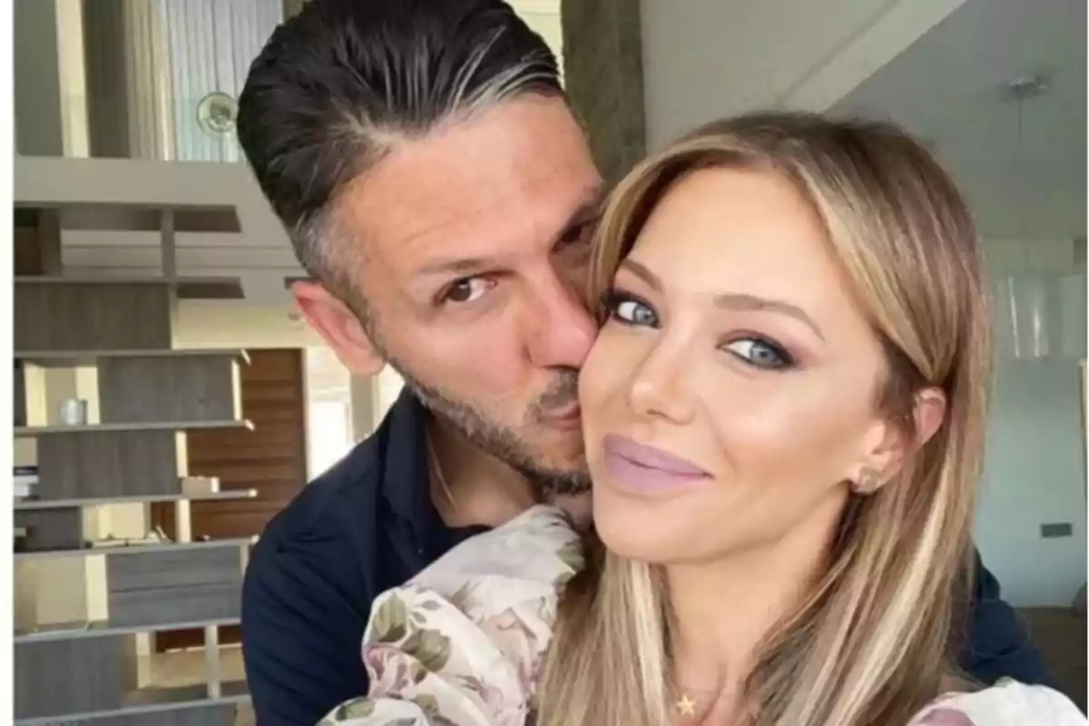 Pareja tomándose una selfie en el interior de una casa mientras el hombre besa la mejilla de la mujer y ambos sonríen
