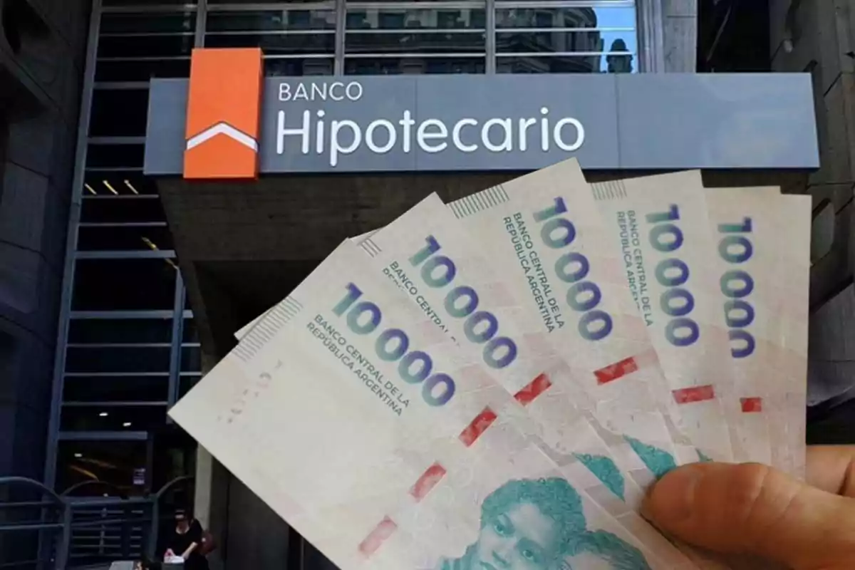 Fachada de un banco hipotecario con una mano sosteniendo varios billetes de diez mil pesos argentinos