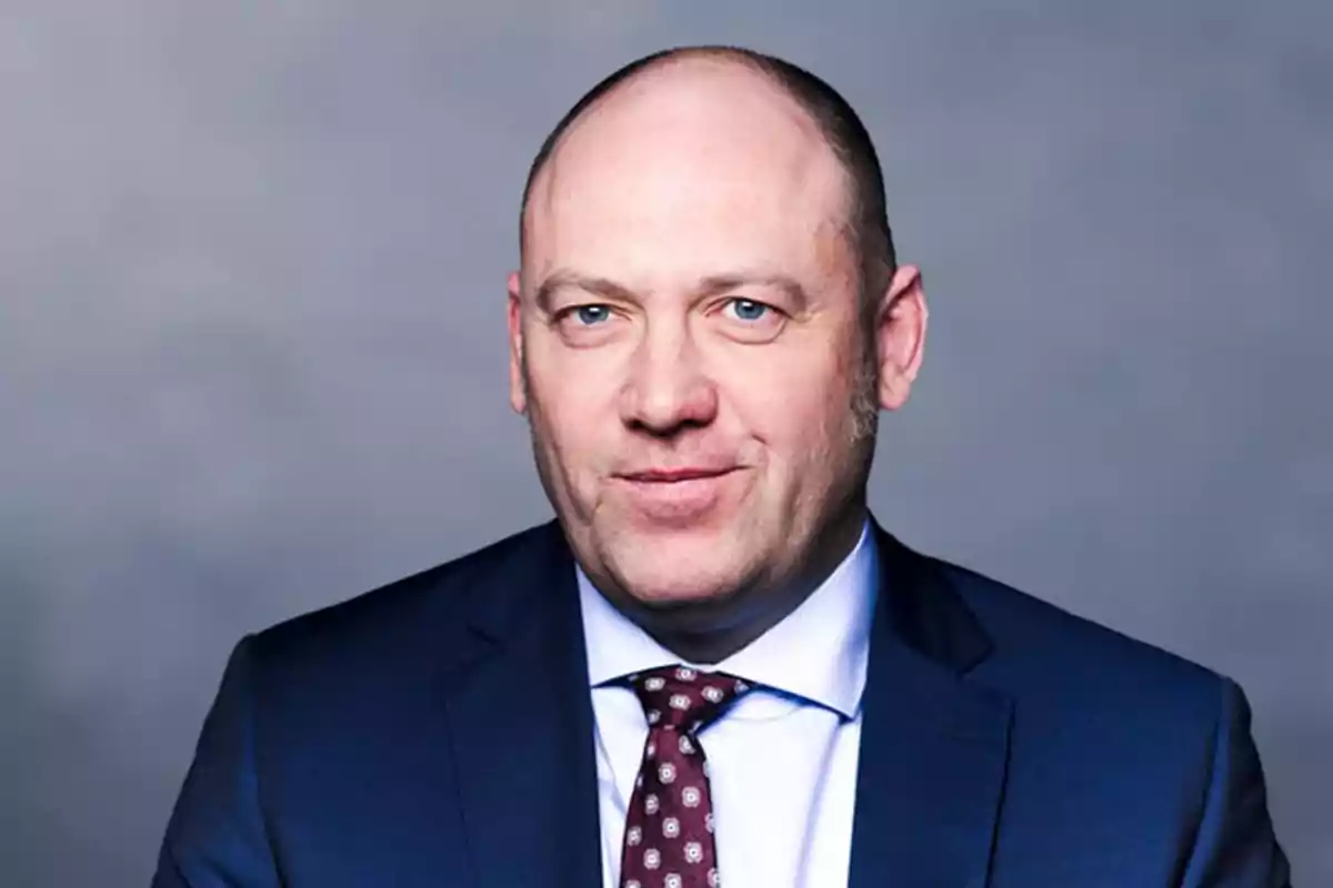 Bald man with light eyes wearing a blue suit and tie with a blurred gray background Bald man with light eyes wearing a blue suit and tie with a blurred gray background