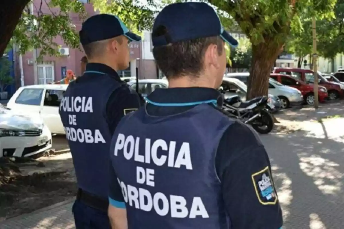 Dos policías de Córdoba de espaldas patrullan una calle arbolada con autos estacionados Dos policías de Córdoba de espaldas patrullan una calle arbolada con autos estacionados