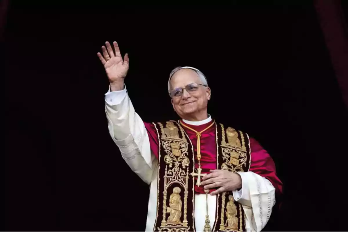 Elderly man in papal attire waving and smiling in front of a dark background