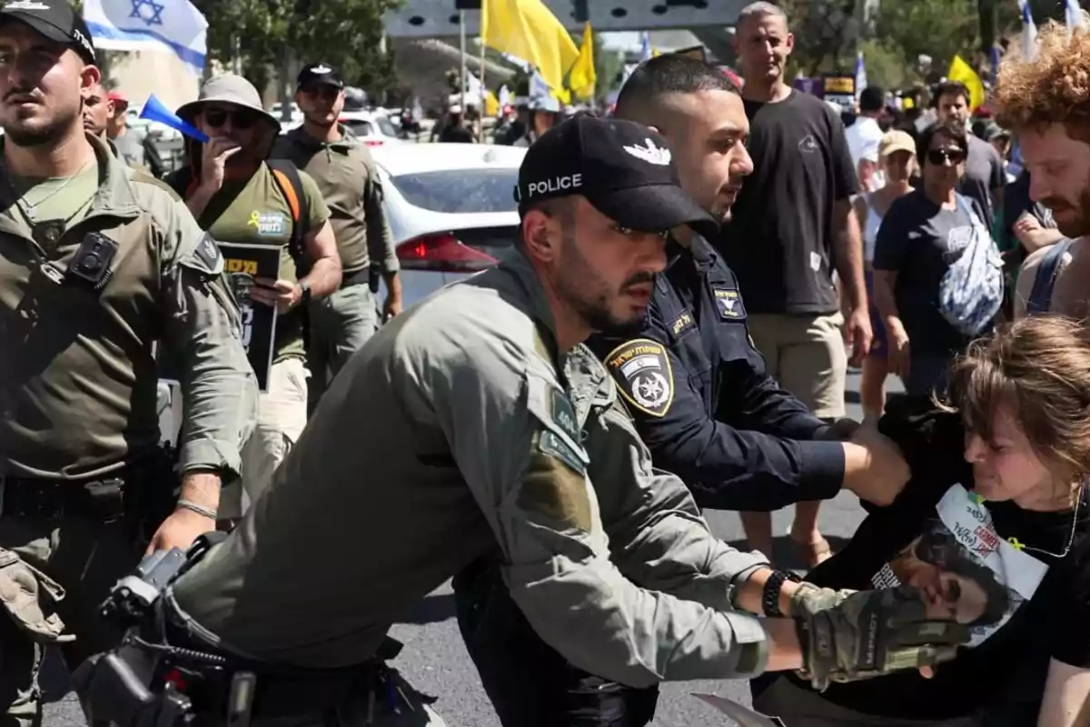 Police detain a protester during a street demonstration while several people watch and wave flags in the background. Police detain a protester during a street demonstration while several people watch and wave flags in the background.