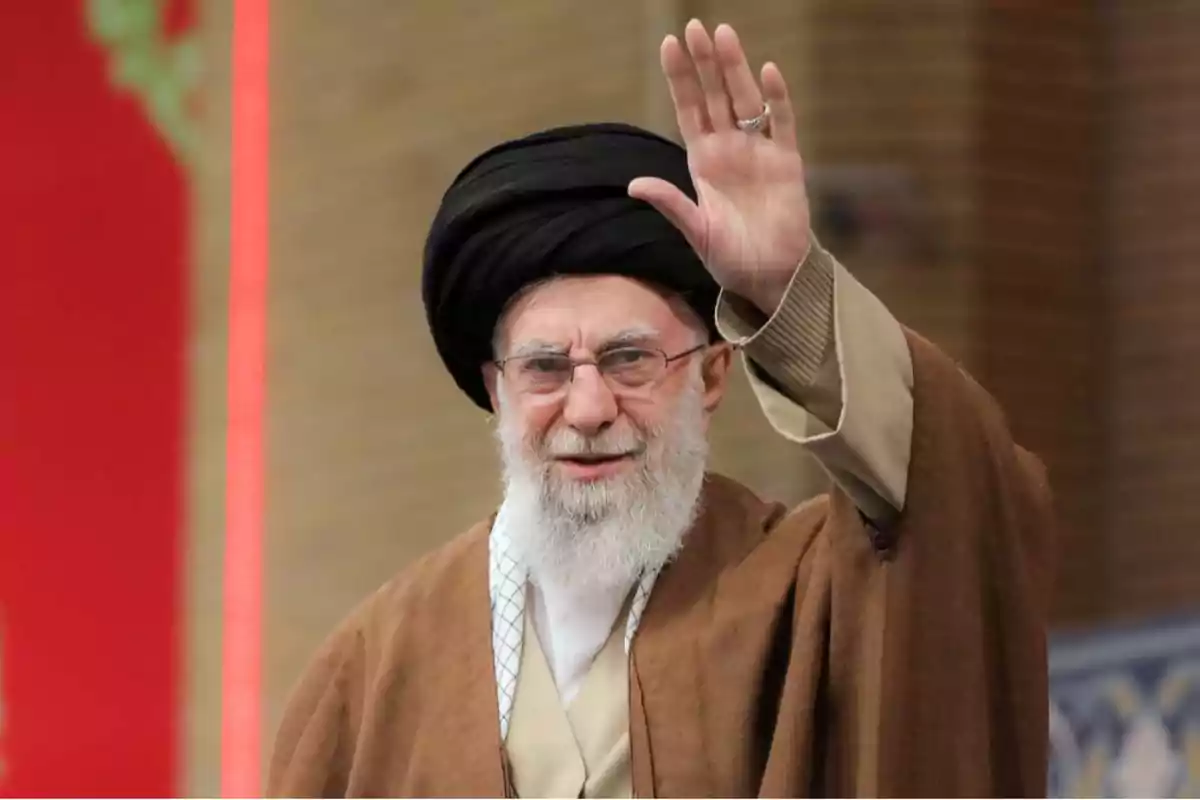 Elderly man with a white beard, wearing glasses and a black turban, dressed in a brown robe and raising his hand in greeting Elderly man with a white beard, wearing glasses and a black turban, dressed in a brown robe and raising his hand in greeting