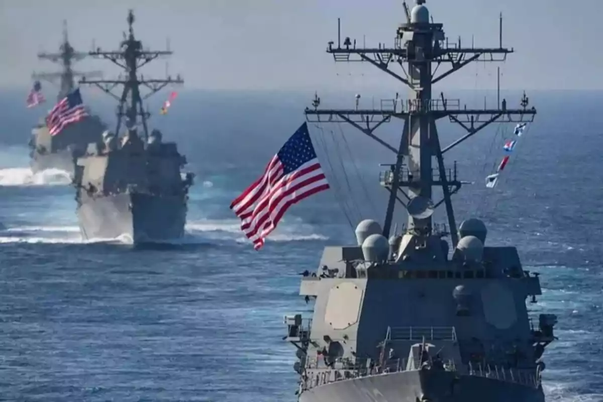 Three warships sail in formation across the sea, flying United States flags. Three warships sail in formation across the sea, flying United States flags.