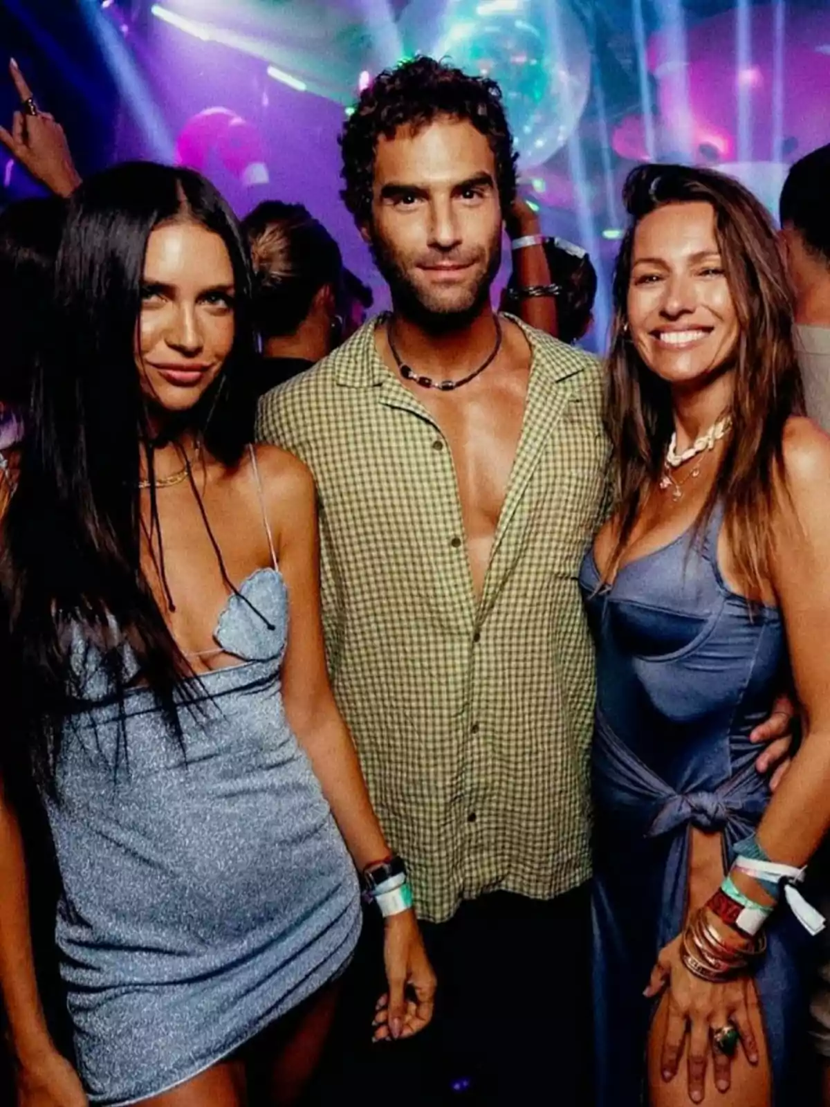 Three people pose smiling in a nightclub with colorful lights and a festive atmosphere. Three people pose smiling in a nightclub with colorful lights and a festive atmosphere.