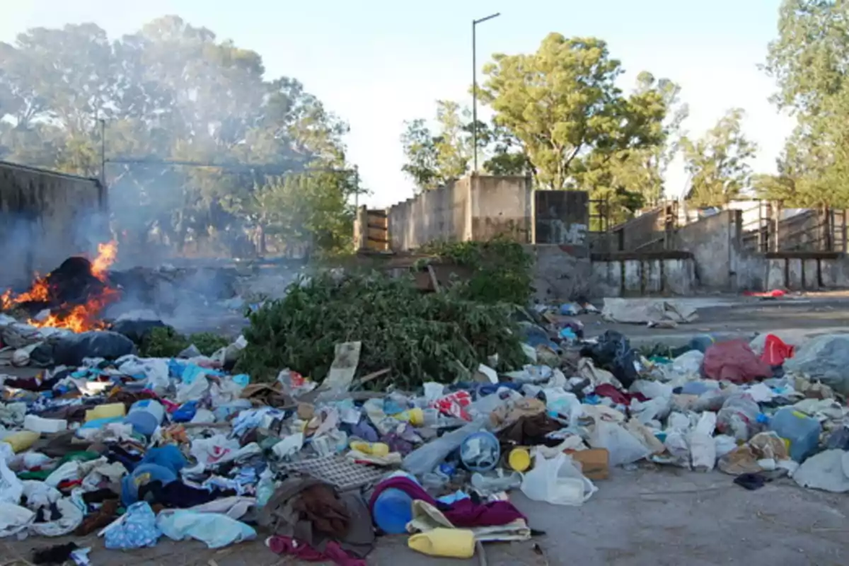 Garbage and waste scattered on an open field with fire and smoke in the background and trees around. Garbage and waste scattered on an open field with fire and smoke in the background and trees around.