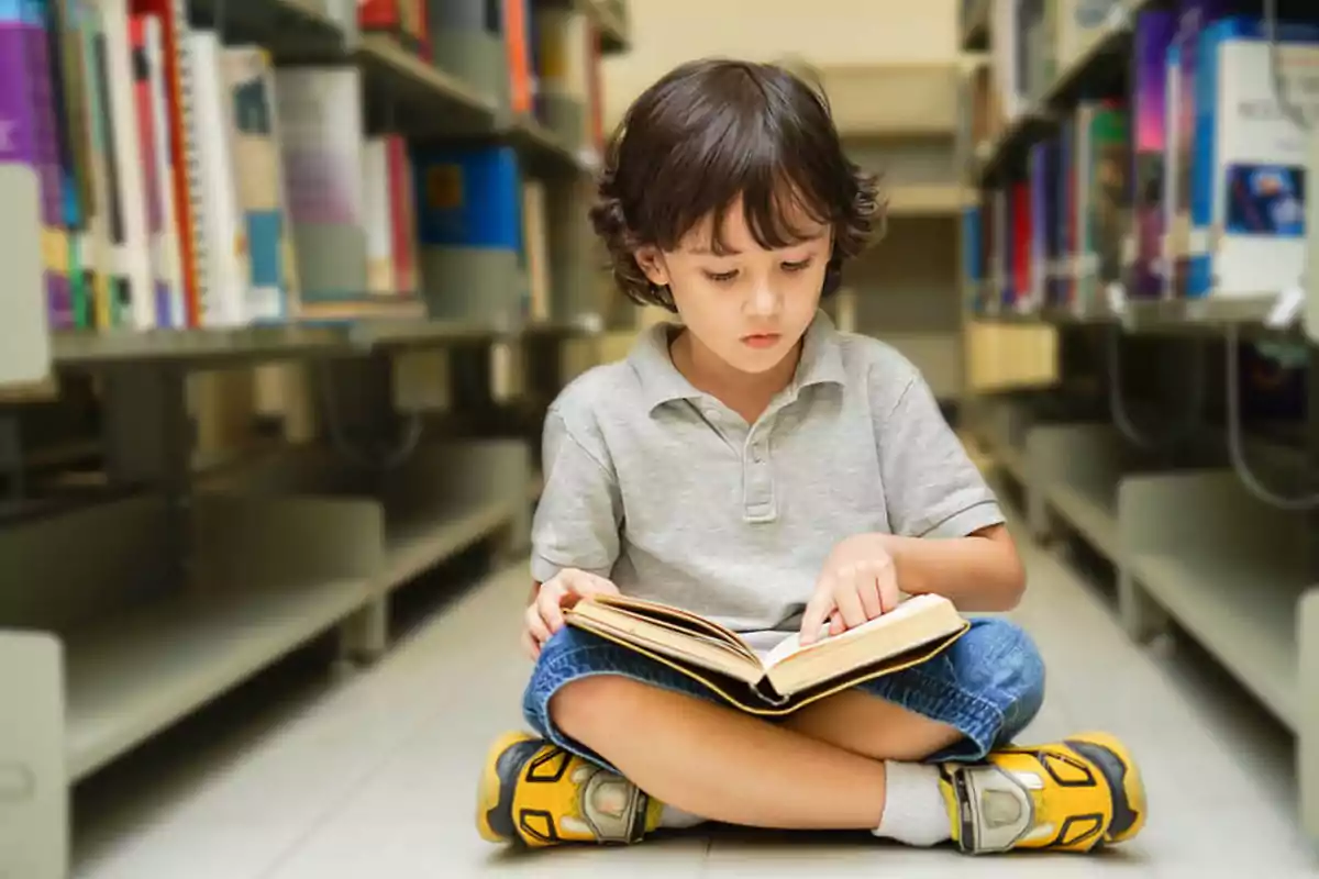 Little boy sitting on the floor of a library reading a book surrounded by shelves full of books Little boy sitting on the floor of a library reading a book surrounded by shelves full of books