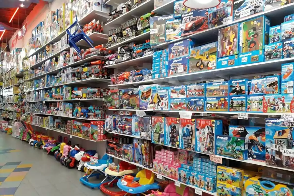 Estanterías llenas de juguetes y cajas de juegos en una tienda, con triciclos y andadores alineados en el suelo