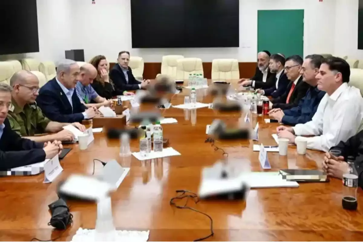 Reunión de varias personas sentadas alrededor de una mesa de madera en una sala de conferencias, con documentos, botellas de agua y vasos sobre la mesa
