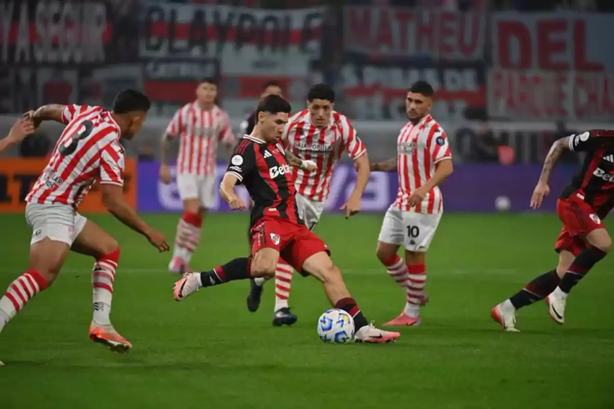 Soccer players from two teams compete for the ball during a match in a stadium full of spectators. Soccer players from two teams compete for the ball during a match in a stadium full of spectators.