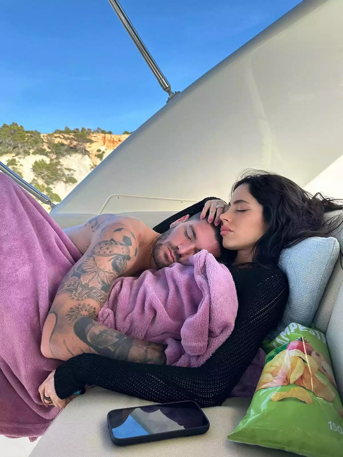 Pareja abrazada descansando en un yate cubierta con una manta rosa junto a una bolsa de papas y un teléfono móvil Pareja abrazada descansando en un yate cubierta con una manta rosa junto a una bolsa de papas y un teléfono móvil